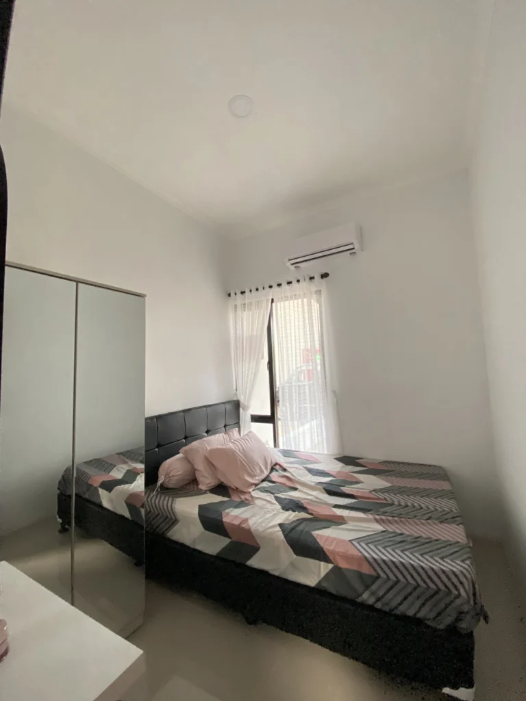 Kamar tidur utama di Pesona Arum Residence Bekasi dengan desain modern minimalis, kasur besar, lemari cermin, dan jendela pencahayaan alami.