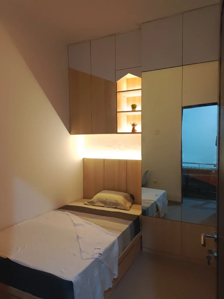 Kamar tidur single dengan desain modern minimalis dilengkapi lemari dan penerangan hangat.